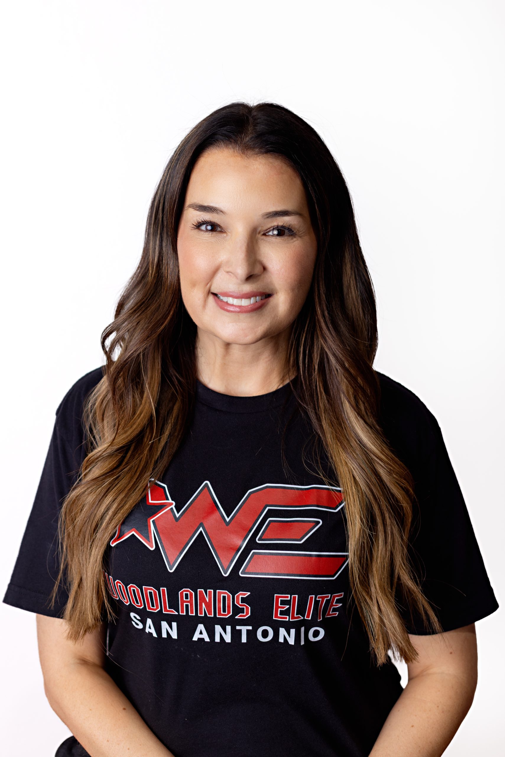 Smiling woman with long brown hair wearing a black T‑shirt with a large red WE graphic and white text, against a white background (San Antonio, TX design on shirt).
